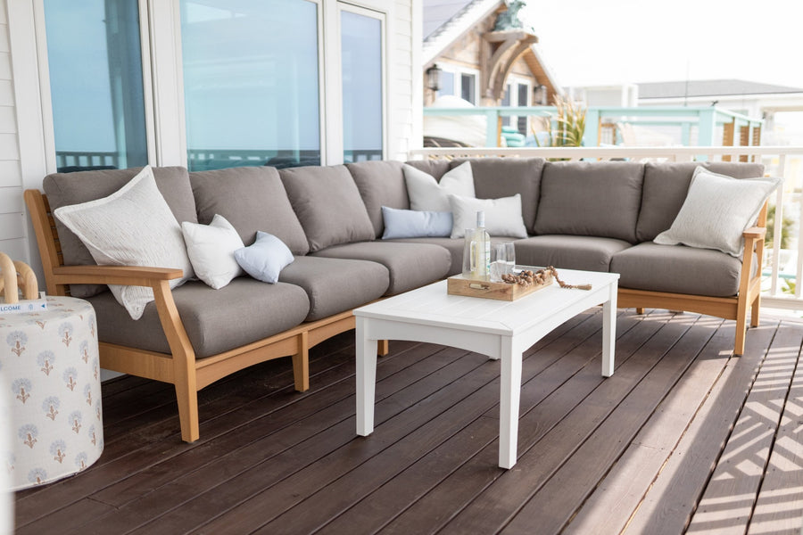 classic-Sectional in Natural Teak with cushions in Play Mushroom, complemented by throw pillows in various shades including Canvas Skyline and Palm Springs Sand, paired with a white coffee table on a wooden deck overlooking a coastal view.