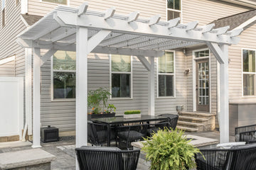 Elegant white pergola with black outdoor seating, set on a stone patio beside a modern home, creating a sophisticated and inviting outdoor living space.